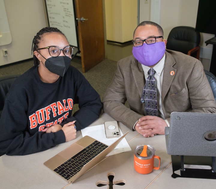 Student sits and talks with completion coach at a table with two laptop computers