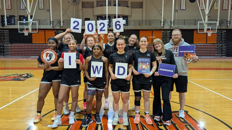 The Buffalo State Women's Basketball team holding a sign that spells IWD 2026