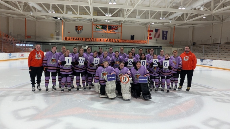 The Buffalo State Women's Hockey Team holding a sign that spells IWD 2026