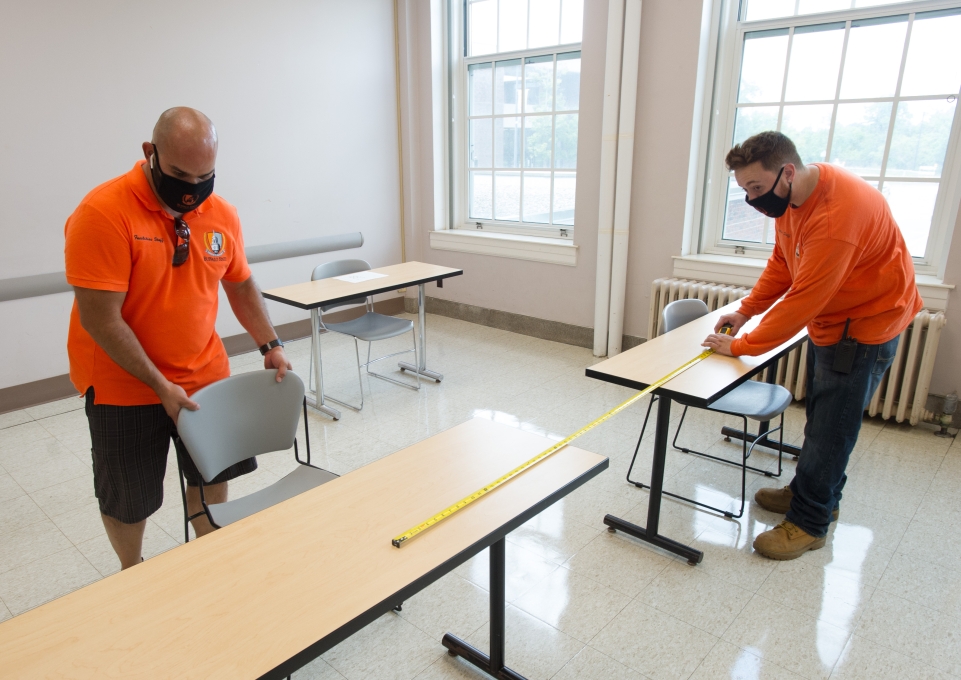 Workers use a tape measure to gauge distance between desks 
