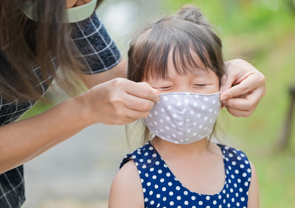 Young girl grimacing as adult puts mask on her face