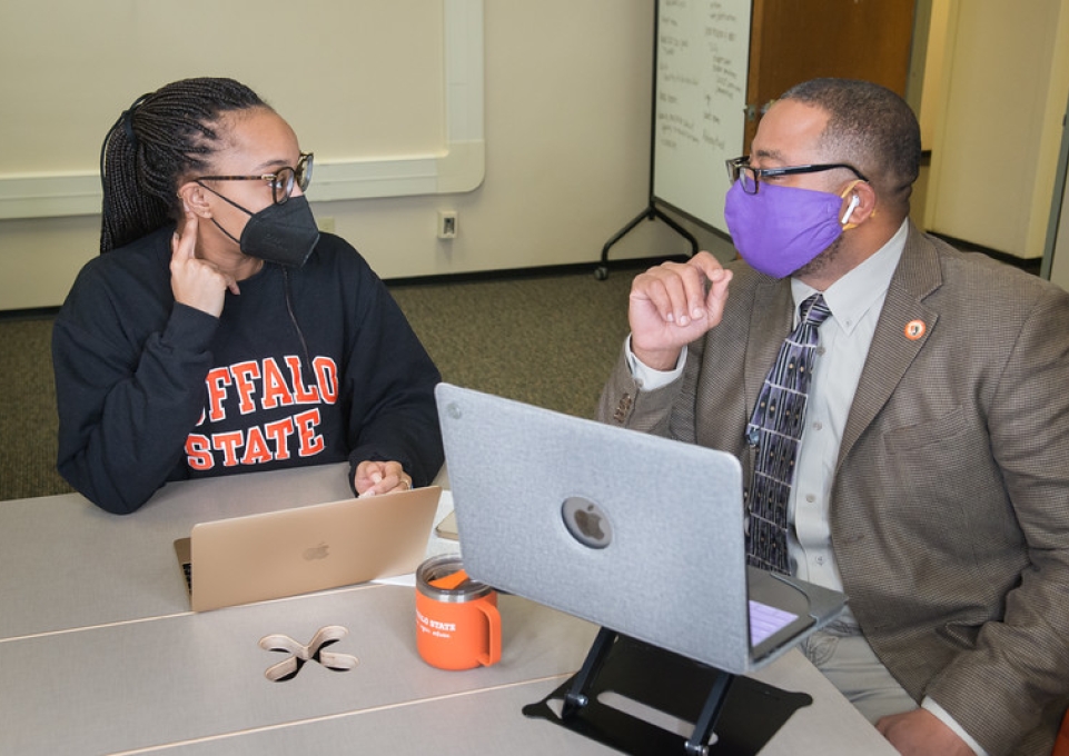 Student sits and talks with completion coach at a table with two laptop computers