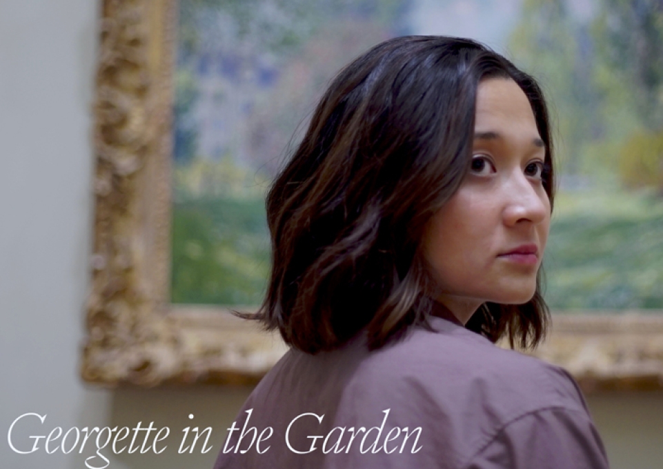 Screen shot from the film Georgette showing a woman with turned head standing before a mounted painting