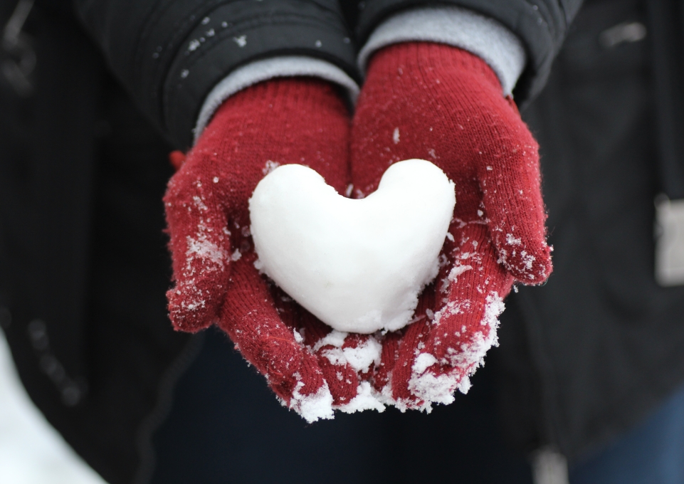 Gloved hands holding a heart-shaped snowball