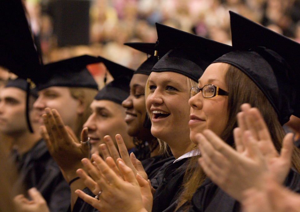 Students in caps and gowns applauding at commencement 