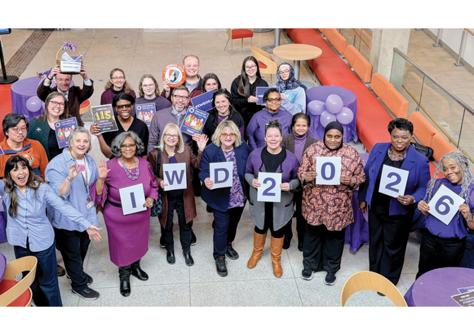 A group of male and female faculty and staff members, including interim president Bonita Durand, wearing purple and holding a sign that spells IWD 2026