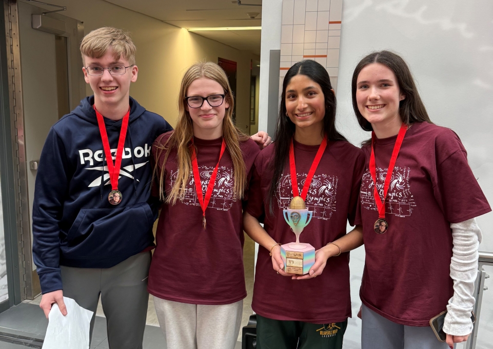 Four high school students, one holding a trophy